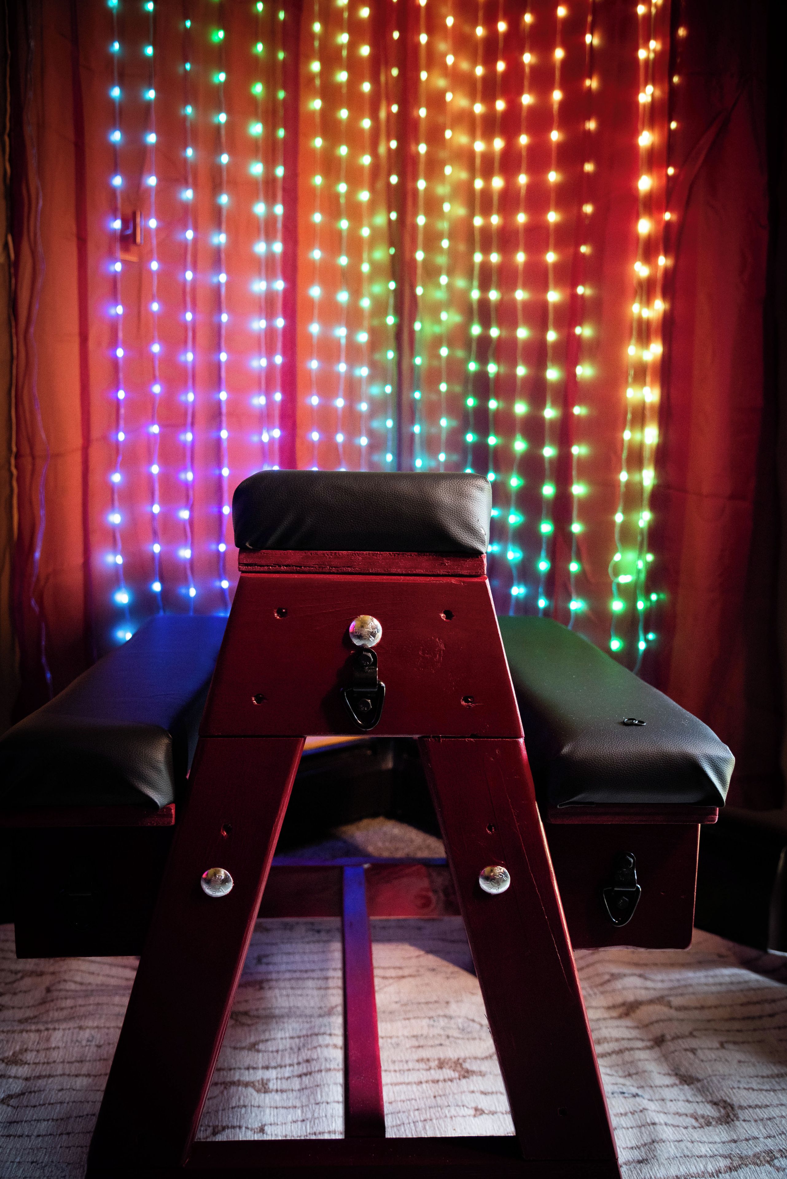 A red bench with a black cushion in front of a curtain with multicolored lights.
