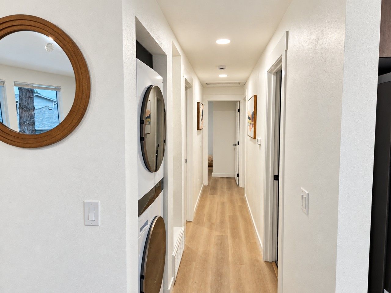 A hallway with a wooden floor, white walls, and a round mirror on the left.