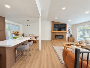 A modern living space with a kitchen area, dining setup, and a seating area with a fireplace.