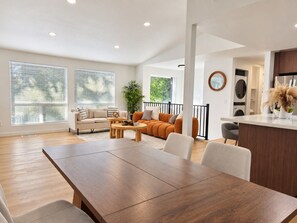 A modern living room with a dining area, a sofa set, and a kitchen in the background. - Modern Kent 3BR/2BA Retreat | Kitchen & Laundry (Kent)