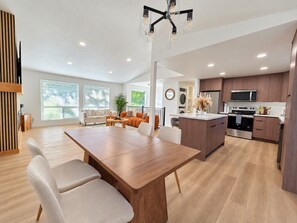 A modern kitchen with wooden cabinets, a central island, and a dining area with a wooden table and chairs. - Modern Kent 3BR/2BA Retreat | Kitchen & Laundry (Kent)