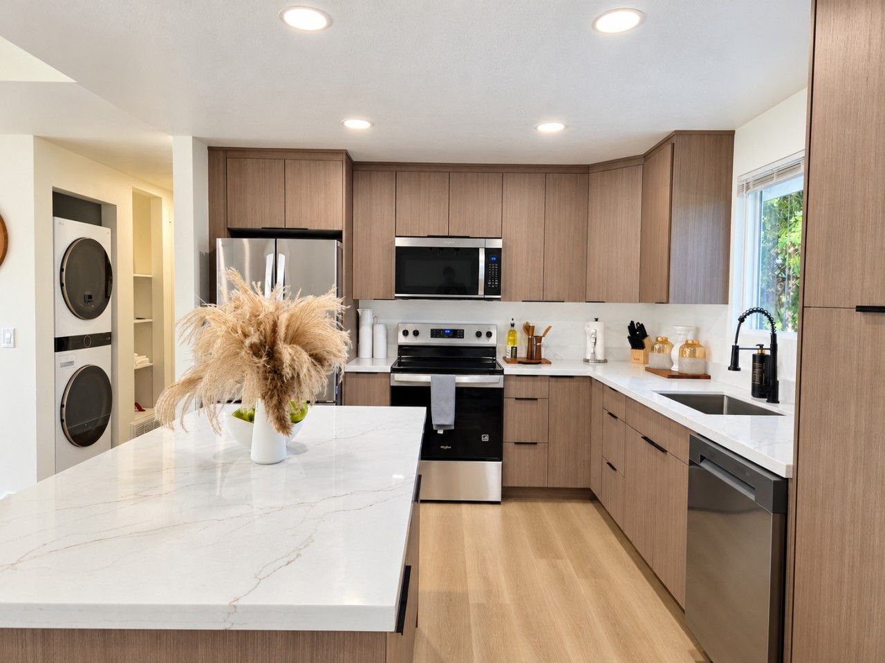 A modern kitchen with a central island, built-in appliances, and wooden cabinetry.