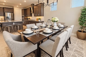 A modern kitchen with dark cabinetry, stainless steel appliances, and a dining area with a long table set for six. - Entire home in Goodyear, Arizona, United States (Goodyear)