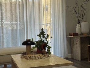 Una habitación con un sofá, una mesa con una planta decorativa, una lámpara y un florero en una estantería.