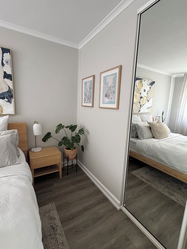 Una habitación de hotel con cama, mesita de noche, lámpara, planta en maceta y una obra de arte enmarcada en la pared.