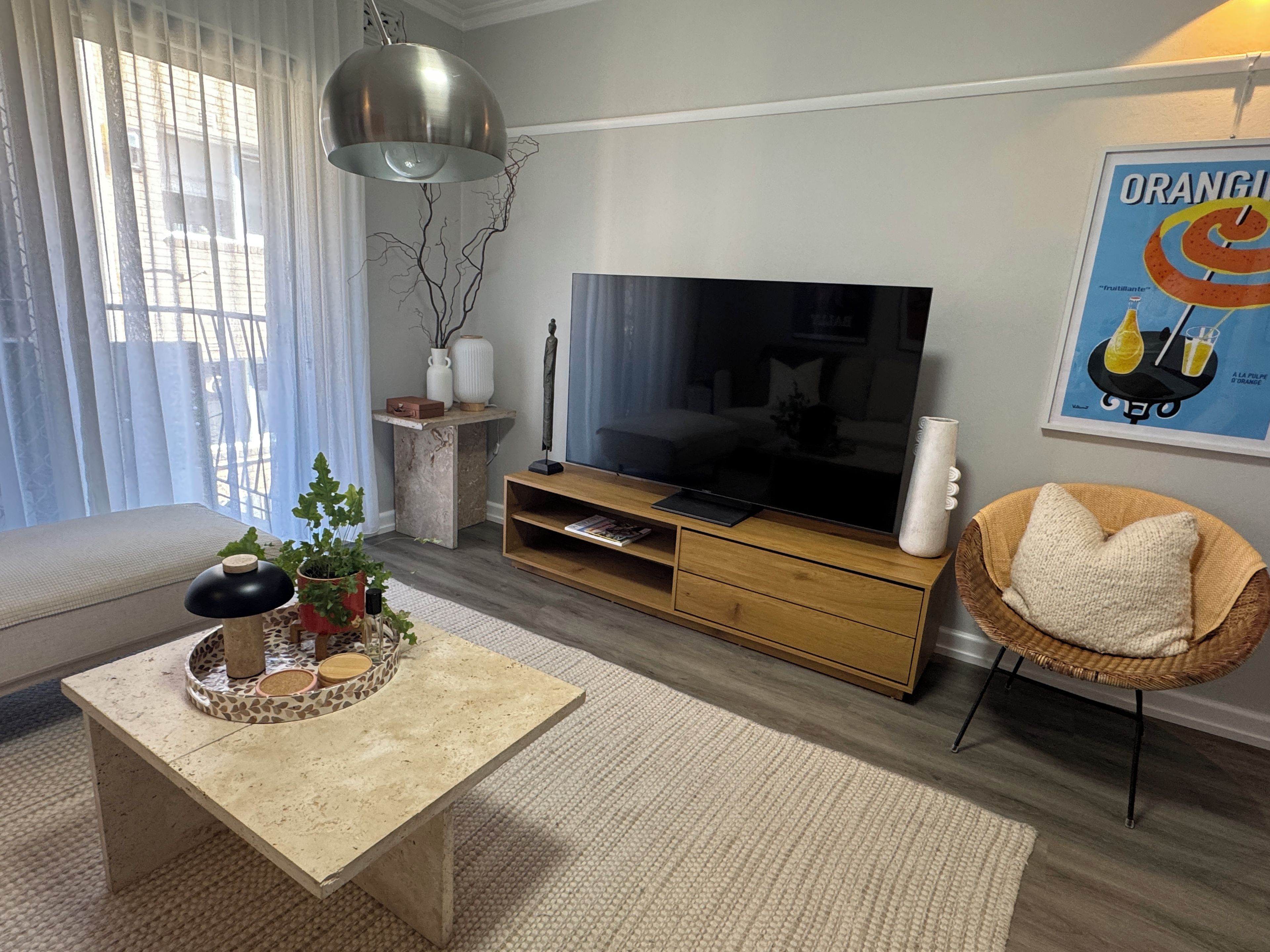 A modern living room with a flat-screen TV, a sofa, a coffee table, and a wicker chair.