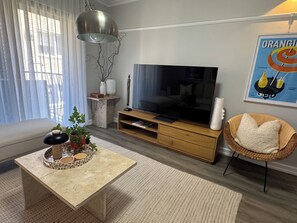 Una sala de estar moderna con un televisor de pantalla plana, un sofá, una mesa de centro y una silla de mimbre.