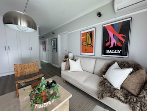 A modern living room with a sofa, a coffee table with a plant, a hanging light fixture, and framed artwork on the wall.