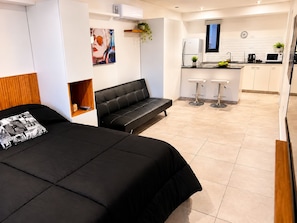 Habitación de hotel moderna con cama, sofá, kitchenette pequeño y baño.