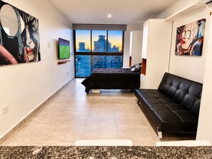 Een moderne slaapkamer met een bed, een zwarte leren bank, een groot raam met uitzicht op de stad en kunstwerken aan de wanden.