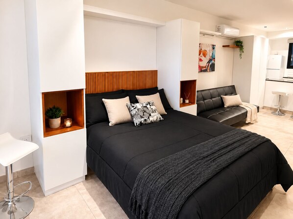 Een moderne slaapkamer met een groot bed, een zithoek en een kitchenette.