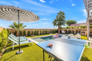 Un espace extérieur avec une piscine, des chaises longues, une table de ping-pong et un bar.