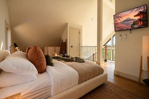 Quarto com cama grande, televisão na parede e vista para a montanha pela janela.