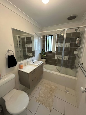 A bathroom with a toilet, sink, mirror, shower, and a small window. - Room-cosy Suburban Townhouse (Brisbane)