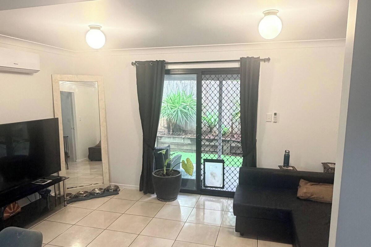 A living room with a tiled floor, a television, a sofa, and a potted plant.