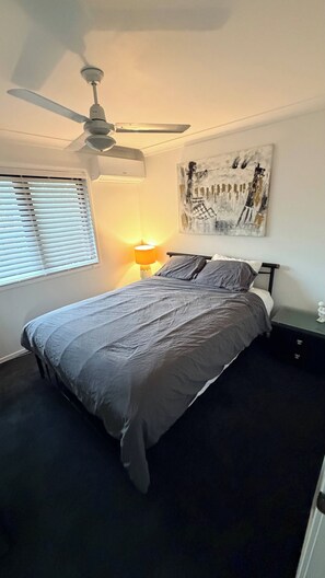 A bedroom with a bed, a ceiling fan, a wall-mounted lamp, a window with blinds, and a painting. - Room-cosy Suburban Townhouse (Brisbane)