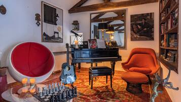 Une pièce comprenant un piano à queue, un fauteuil rouge, une bibliothèque, un jeu d’échecs et une sculpture décorative.