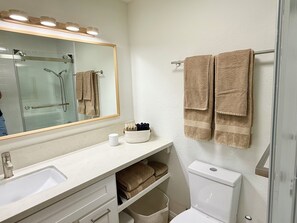 Un baño con lavamanos, espejo, toallero y retrete.