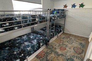 Une chambre avec un lit superposé, une couvre-lit sur le thème de la galaxie, un tapis à motifs et des décorations murales représentant des tortues.