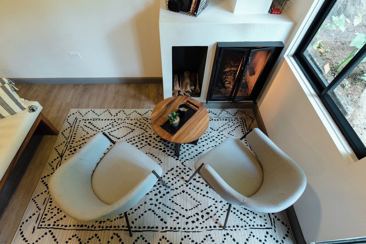 A modern living room with a fireplace, two armchairs, a coffee table, and a patterned rug.