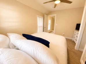 Un dormitorio con cama, ventilador de techo, cómoda y puerta que da a otra habitación.