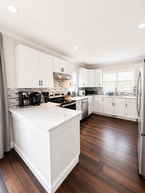 A modern kitchen with white cabinetry, a large island, and a stainless steel refrigerator. - Historic Ashtabula Harbor Home - Stay on the Beach! (Ashtabula)