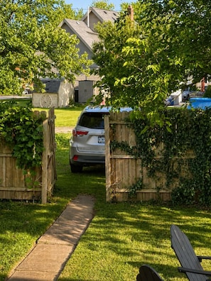 Una entrada de casa con un coche estacionado en el centro, rodeada de una valla de madera y vegetación.