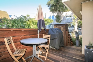 Une terrasse extérieure avec une table ronde et deux chaises, un barbecue et une clôture en bois.