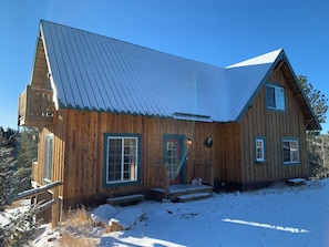 Une cabane en bois avec un toit en métal, un porche à l’avant et un sol recouvert de neige.
