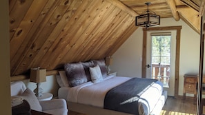 Une chambre avec un plafond en pente, un lit avec de nombreux oreillers, une table de chevet et une commode.