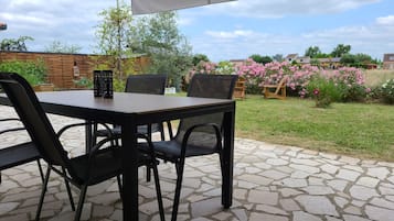 An outdoor patio with a table and chairs, a wooden fence, and a garden with pink flowers.