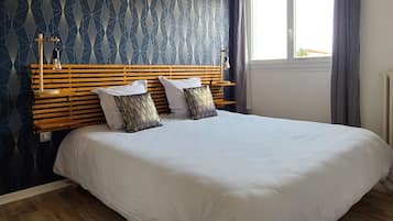A bedroom with a wooden headboard, two pillows, a white bedspread, and a window with curtains.