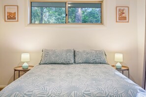 A bedroom with a bed, two bedside lamps, a window with a view of trees, and two framed pictures on the wall. - Quiet Nature Escape Minutes from Myall Lakes & Seal Rocks (Bungwahl)