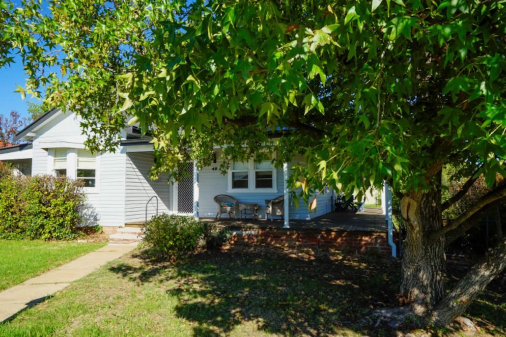 A single-story house with a covered porch and a tree in front.