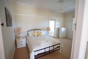 A bedroom with a bed, bedside tables, a wardrobe, and a door leading to another room. - Stella's Place - Boorowa (Boorowa)