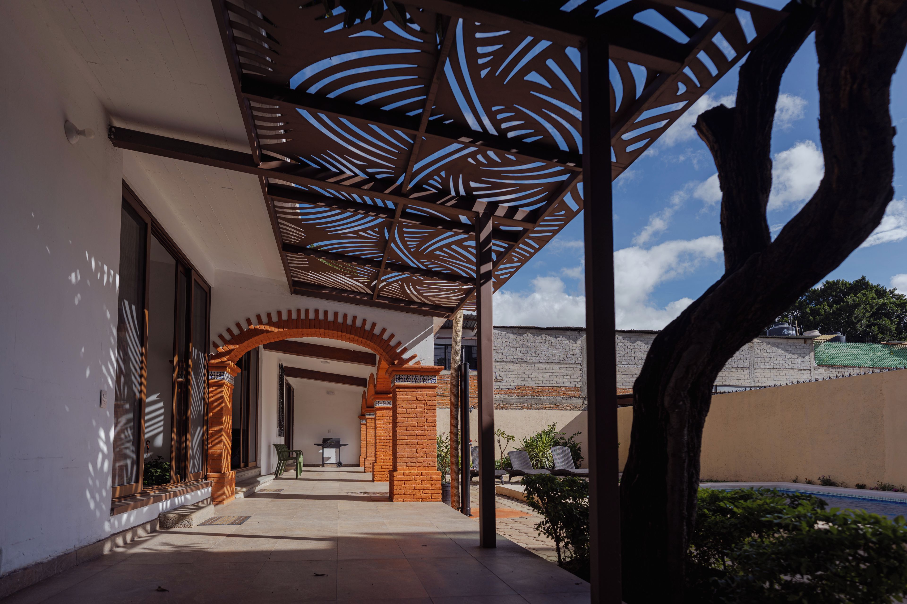 A covered outdoor area with a patterned ceiling, a brick archway, and a view of a building in the background.