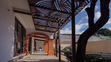 A covered outdoor area with a patterned ceiling, a brick archway, and a view of a building in the background.