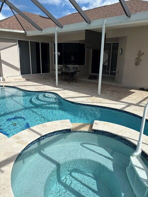 Una piscina con suelo de baldosas, un patio cubierto y una mesa de comedor con sillas.