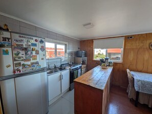 Une cuisine de taille réduite, avec des meubles blancs, un plan de travail en bois et une fenêtre donnant sur un quartier résidentiel.