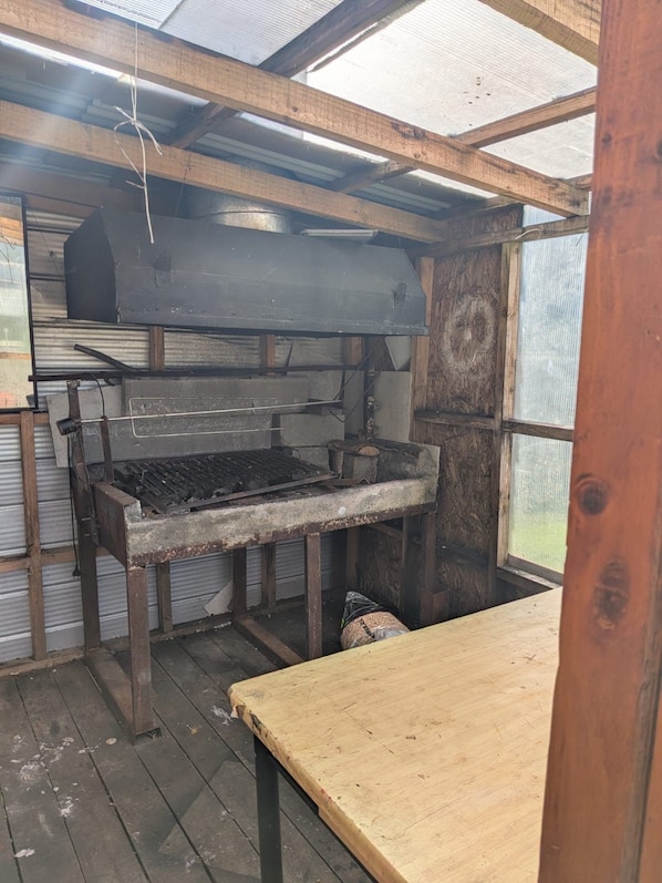 A rustic kitchen with a large industrial stove, wooden beams, and a corrugated metal roof.