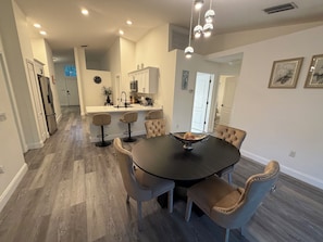 Cocina moderna con armarios blancos, una isla central y un comedor con una mesa redonda y sillas acolchadas.
