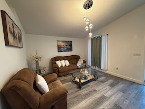 A living room with a brown sofa, a glass coffee table, and a painting on the wall. - 3-bedroom house in nice Land O' Lakes with cool AC (Land O' Lakes)