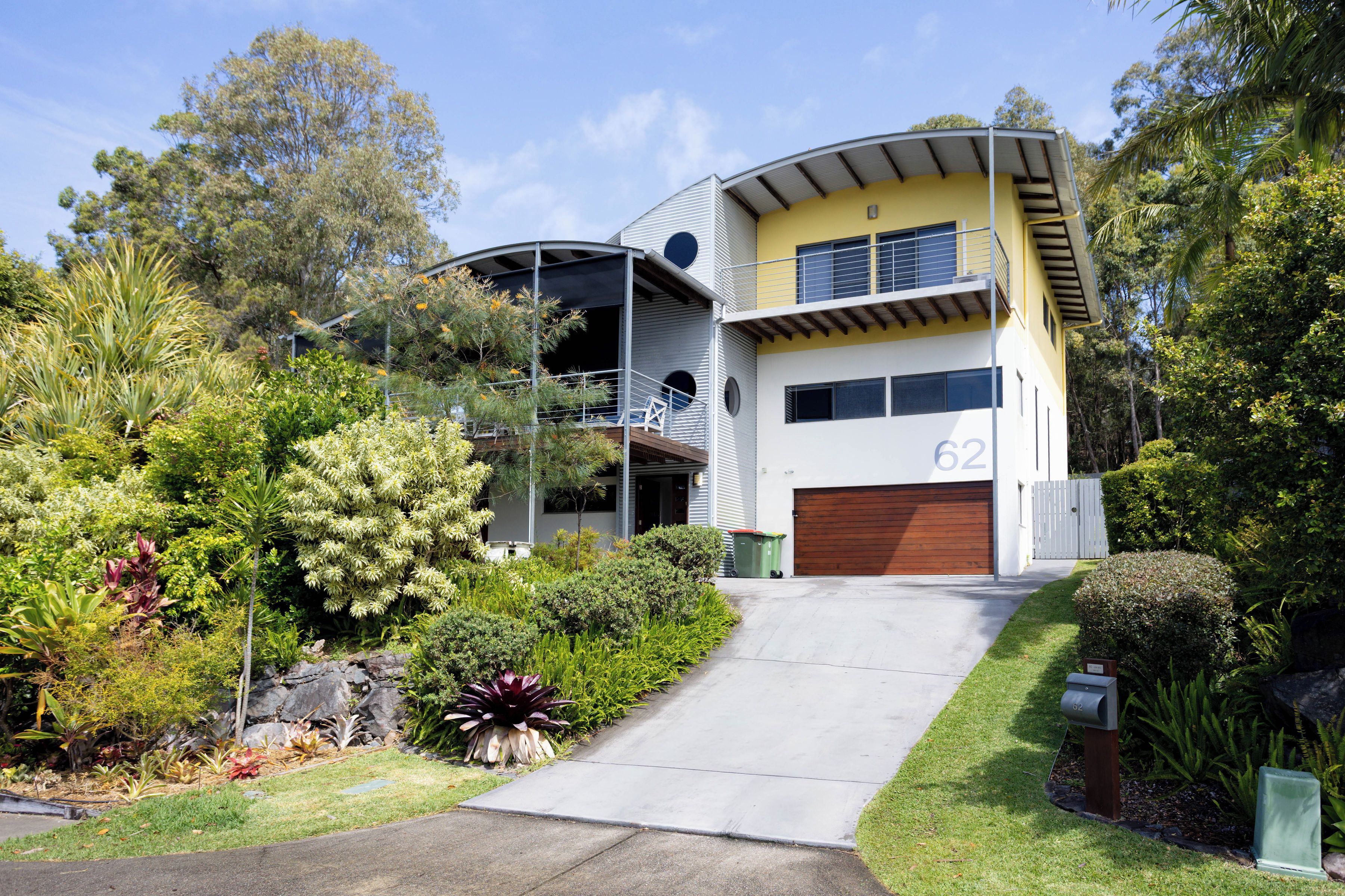 A two-story residential building with a garage, surrounded by lush greenery and a well-maintained lawn.