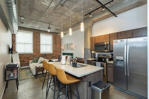 A modern kitchen with a stainless steel refrigerator, a microwave, and a coffee maker. There is a bar area with stools and a sink. - Modern Studio in Downtown DSM + Free Parking + Gym + Workspace (Des Moines)