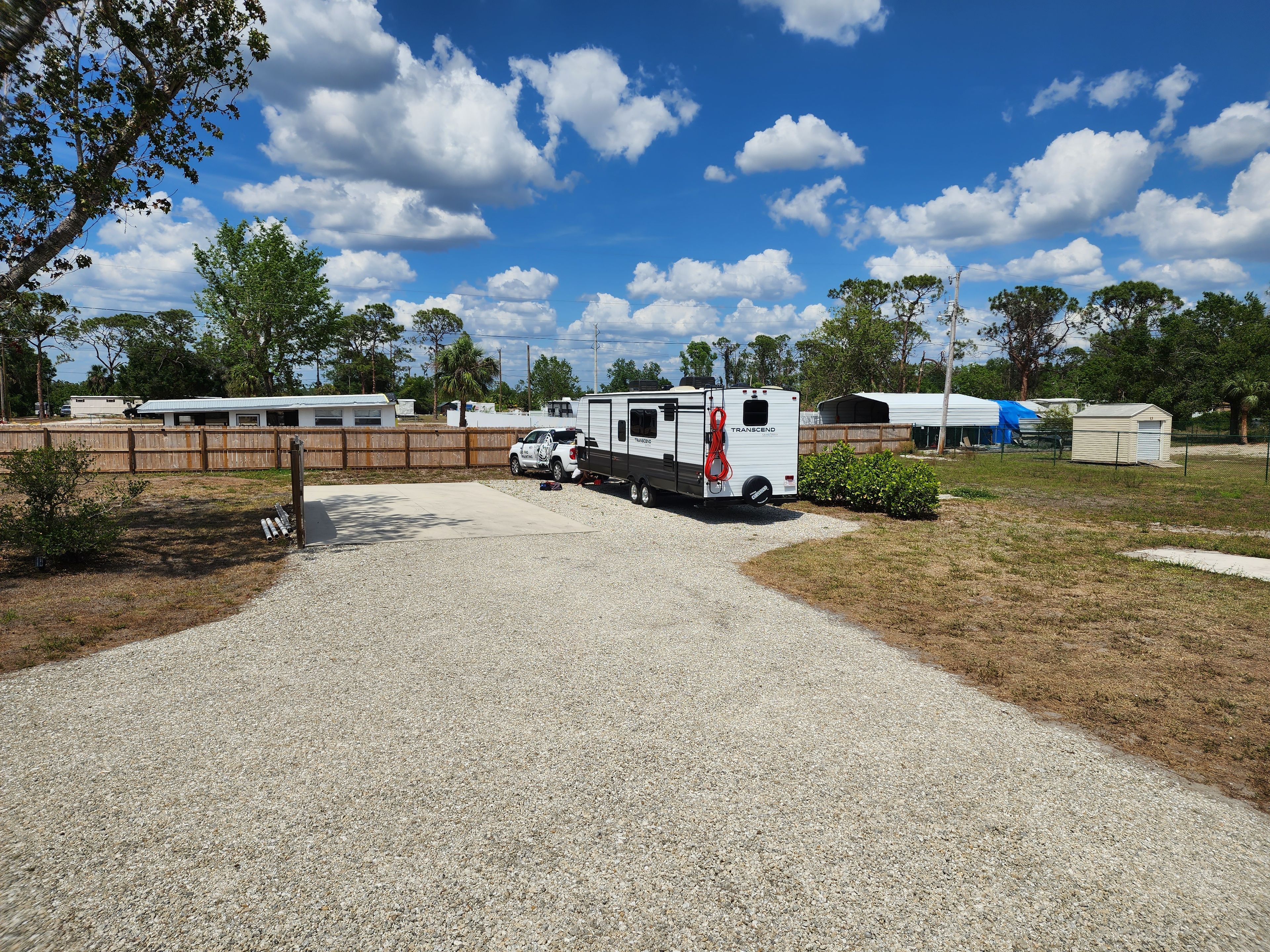 A gravel parking area with a white RV and a pickup truck.