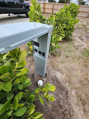 A utility box with electrical outlets and switches, surrounded by green foliage. - Beautiful campground in nice North Fort Myers location Behind my house (North Fort Myers)