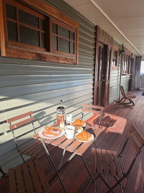 Eine Holterrasse mit einem Tisch, gedeckt für eine Mahlzeit, inklusive Croissants und einer Kaffeekanne.
