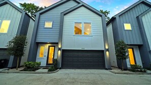 Un immeuble résidentiel moderne à deux étages, doté d’un garage, d’une porte d’entrée et d’un petit espace porche.