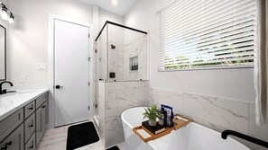 Un baño moderno con ducha envuelta en vidrio, una bañera blanca y una ventana con persianas.