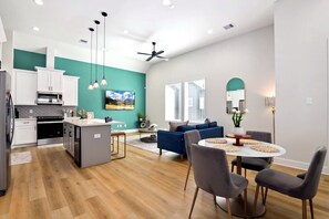 Une cuisine moderne avec des meubles blancs, un îlot central et un coin repas comprenant une table ronde et des chaises.